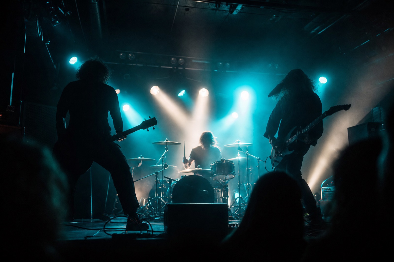 Banda de rock en silueta sobre un pequeño escenario de club bajo luz de contra cian